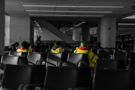 Tres trabajadores con chaleco reflectante sentados en la sala de espera de un aeropuerto. Photo by Austin on Unsplash