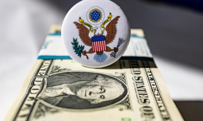 Chapa con el sello de los EE. UU. encima de un fajo de billetes de dólar. Photo by Marek Studzinski on Unsplash