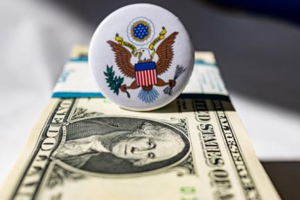 Chapa con el sello de los EE. UU. encima de un fajo de billetes de dólar. Photo by Marek Studzinski on Unsplash