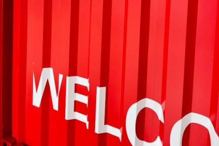 Contenedor de mercancías rojo con el rótulo "WELCO(ME)" en blanco. Photo by Andrii Leonov on Unsplash