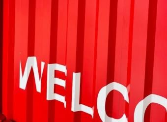 Contenedor de mercancías rojo con el rótulo "WELCO(ME)" en blanco. Photo by Andrii Leonov on Unsplash